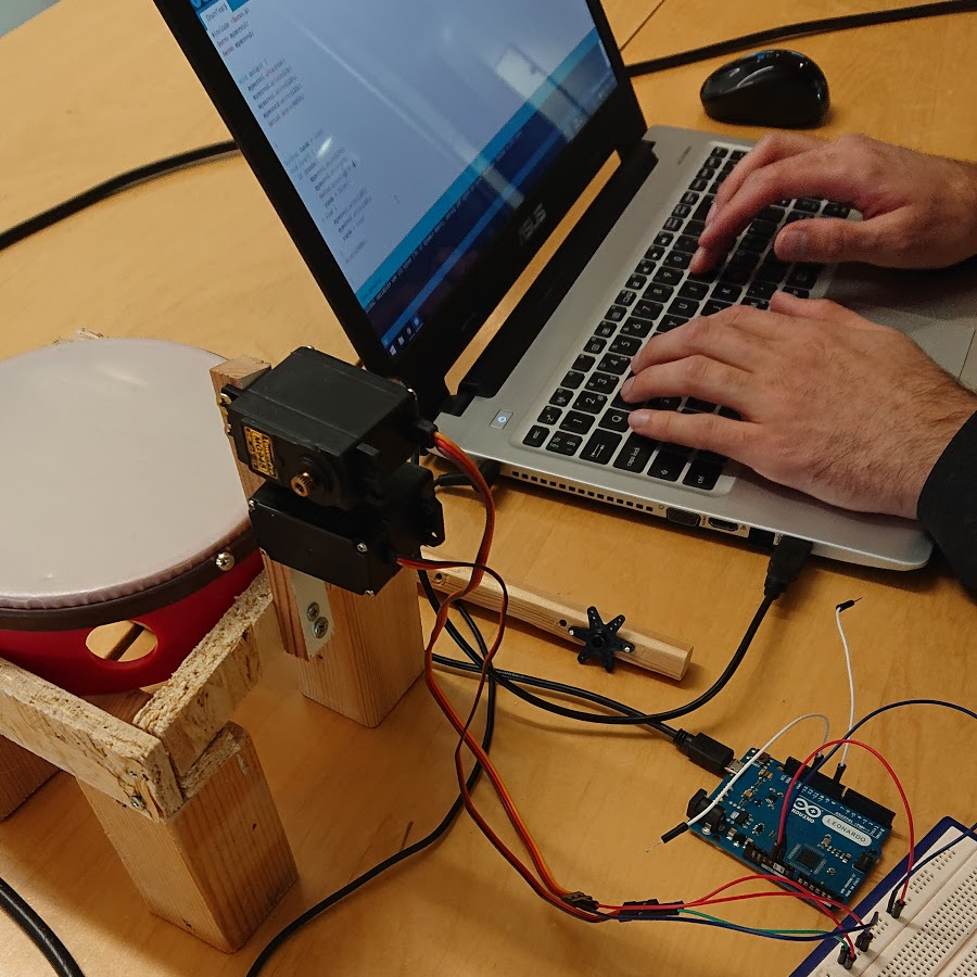 A photo of a robotic drum next to a laptop that someone is writing code on.